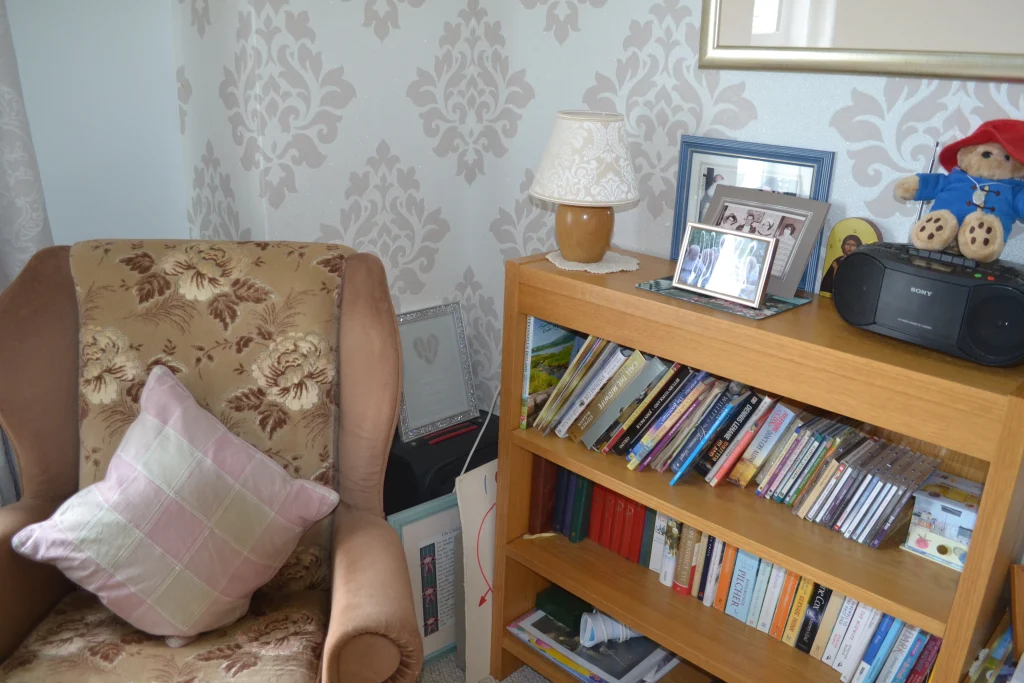 An armchair beside a bookshelf of books and CDs in a resident’s room at Chatsworth