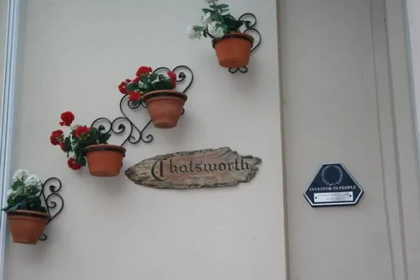 The Chatsworth name sign by the entrance, with potted geraniums and an Investors in People plaque